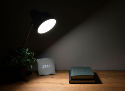 Lampe beleuchtet zwei Bücher und eine digitale Uhr auf Holzunterlage